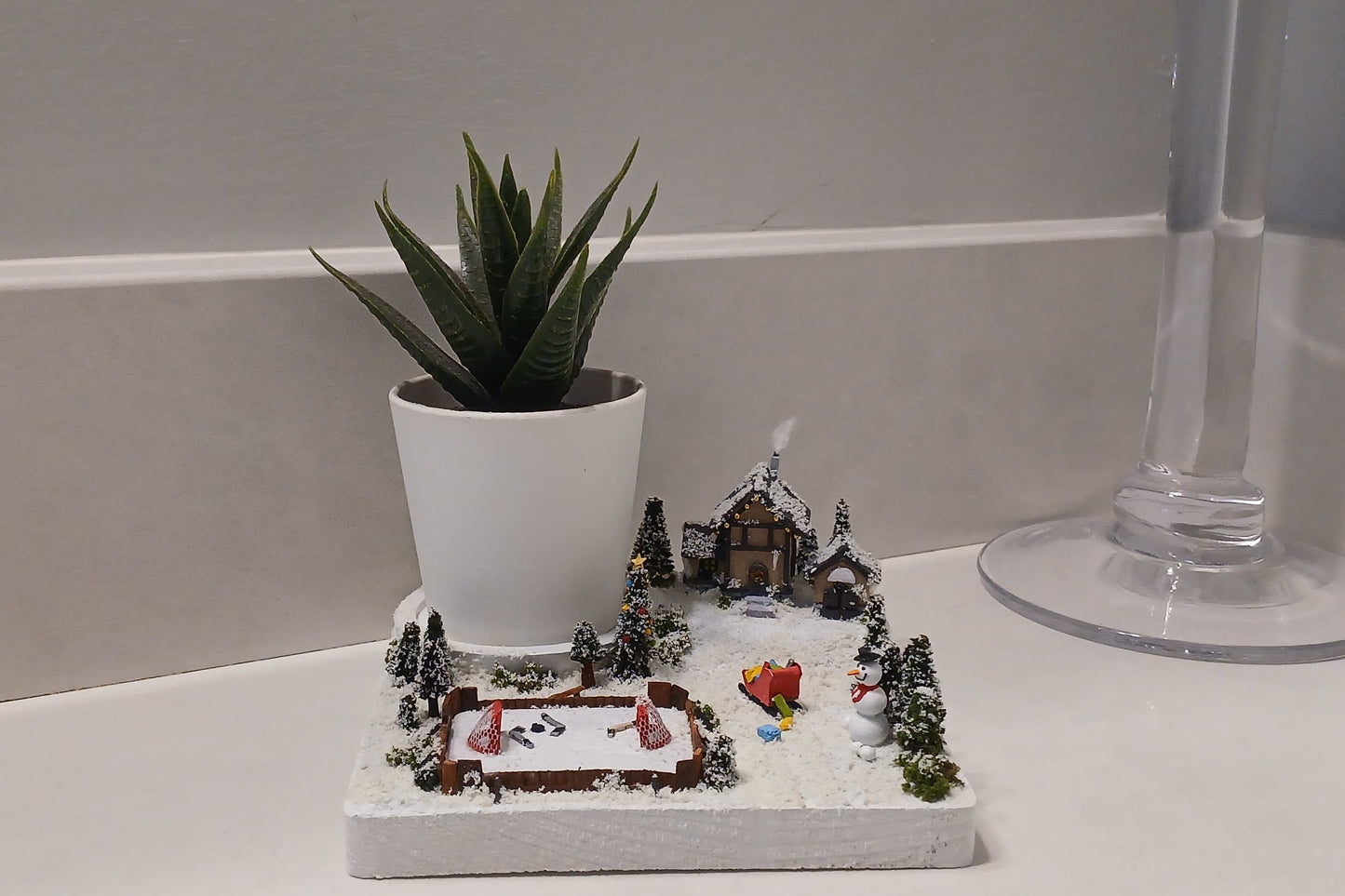 Miniature Ice Rink with Snowman, Sleigh of presents, white snow capped pine trees and a warm chalet. Pot holder, model display, candle holder, diorama.