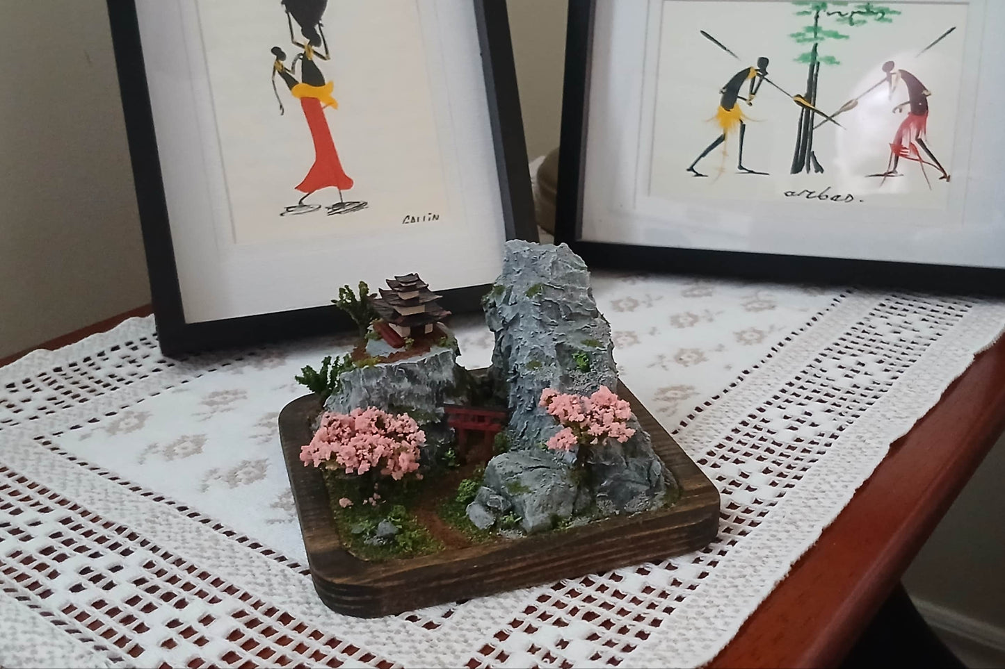 Miniature dirt path under a Torii Gate up a rock face mountain towards a shrine with cherry trees and foilage