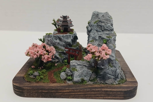 Miniature dirt path under a Torii Gate up a rock face mountain towards a shrine with cherry trees and foilage